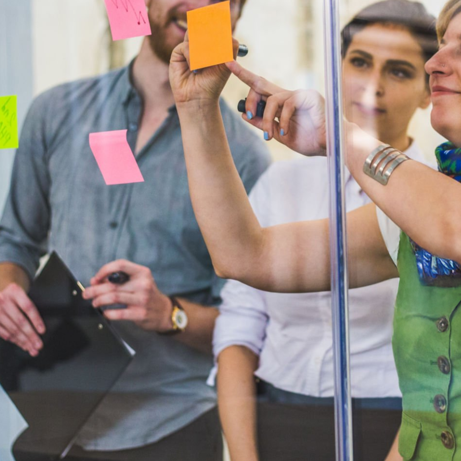 People collaborating and writing on sticky notes on a glass wall in an office setting.