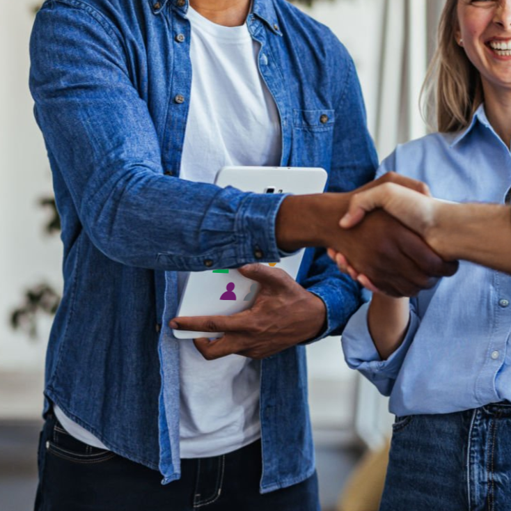 Two people shaking hands indoors, one holding a smartphone, with smiling faces.