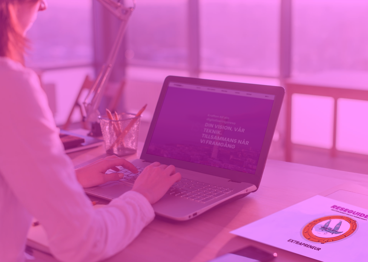 A person working at a desk with a laptop, a glass of pencils, a desk lamp, and a research guide titled 'Reseguide' on an adjacent paper.