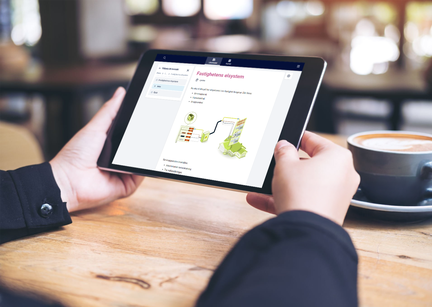 Person holding a tablet displaying a diagram of a property management system, sitting at a wooden table with a cup of coffee nearby.