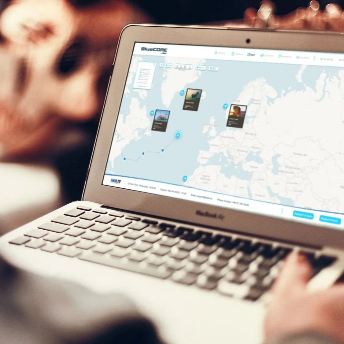 Close-up of a person holding a MacBook laptop displaying a world map and travel routes on the screen.