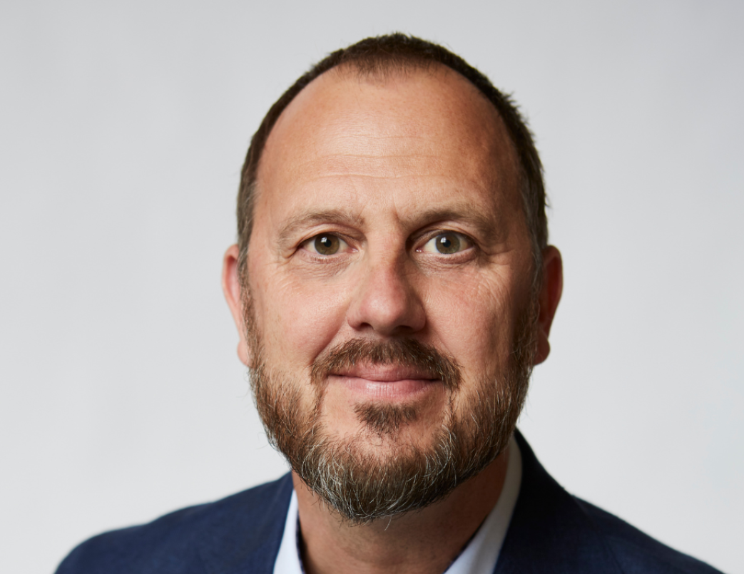 Close-up portrait of a middle-aged man named Peter with a beard, wearing a navy blazer and light-colored shirt, against a plain white background. Despite being 50+ years he looks quite energetic.