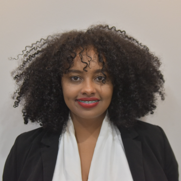 A woman with curly black hair wearing a black blazer and white blouse smiling at the camera.