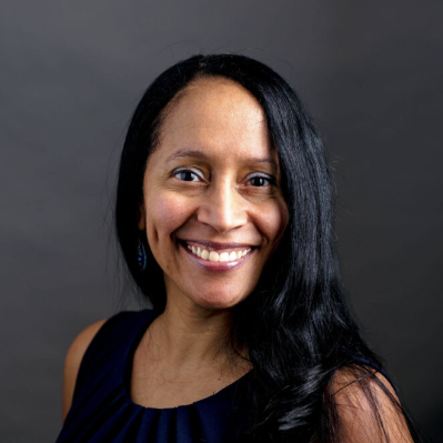 Woman with long black hair and a bright smile, wearing a black sleeveless top, against a dark gray background.