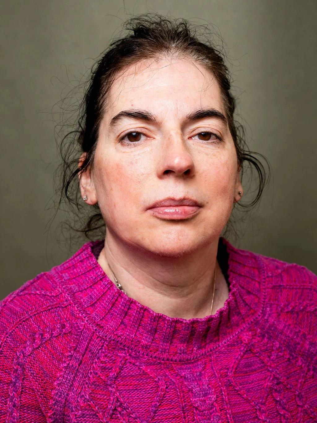 A woman with dark hair pulled back, and wearing a bright pink knitted sweater.