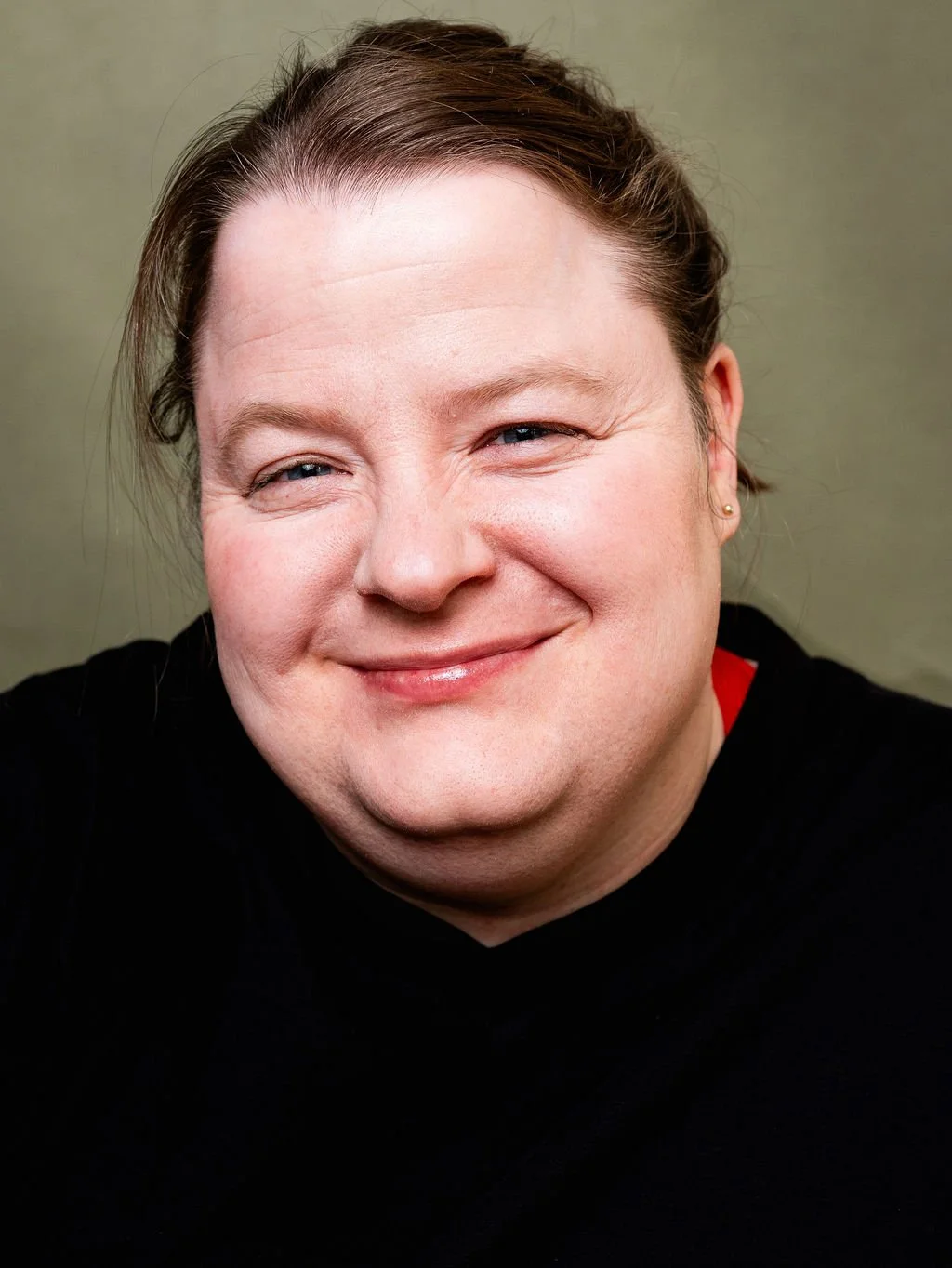 Close-up portrait of a smiling woman, blue eyes, and brown hair pulled back, wearing a black top.