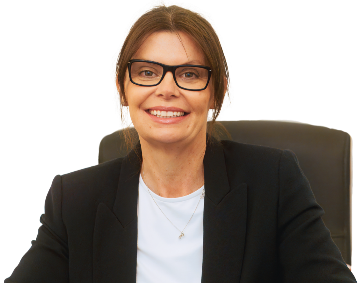 A woman with glasses and brown hair sitting in a black office chair, smiling, wearing a black blazer and white top.