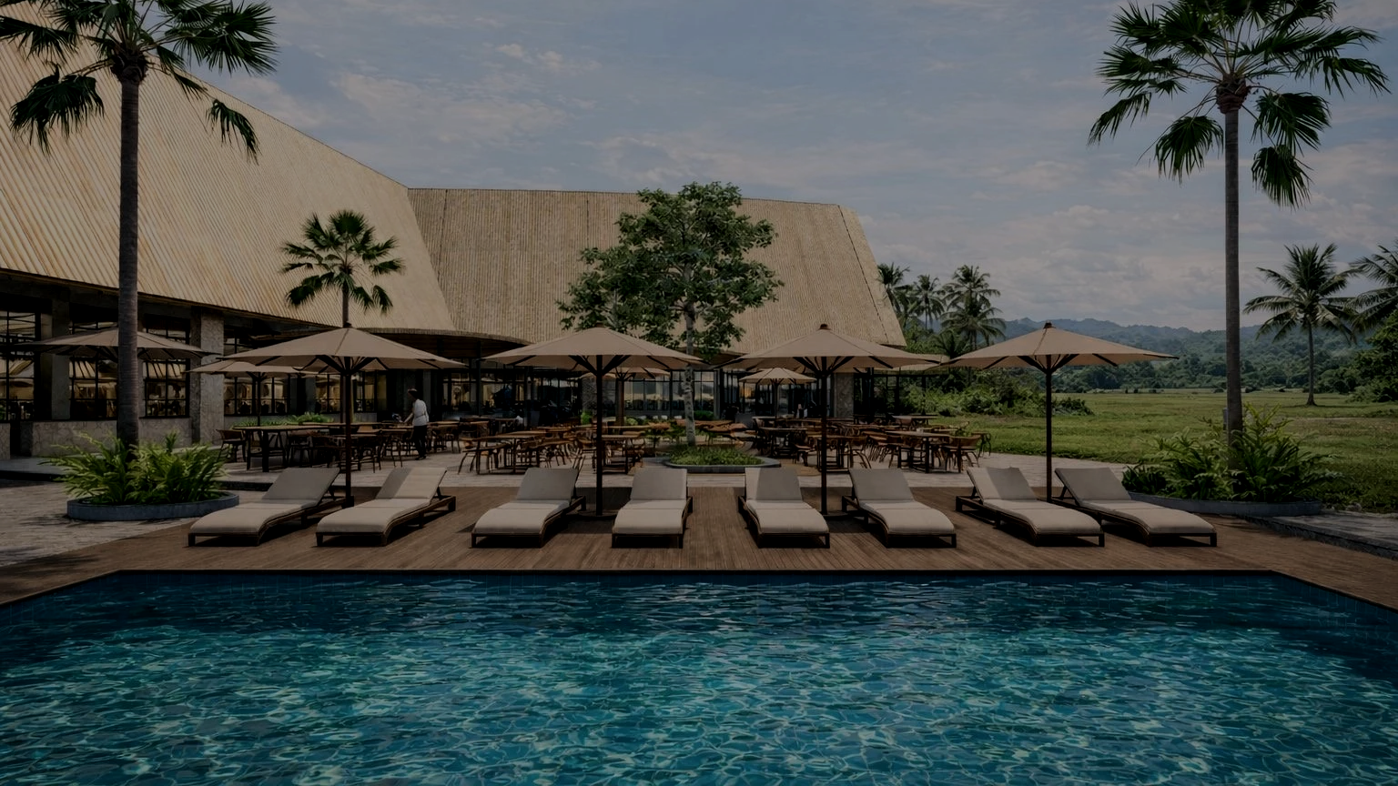 An aerial view of a swimming pool with a person floating on their back, surrounded by lounge chairs and umbrellas, with greenery and trees around.