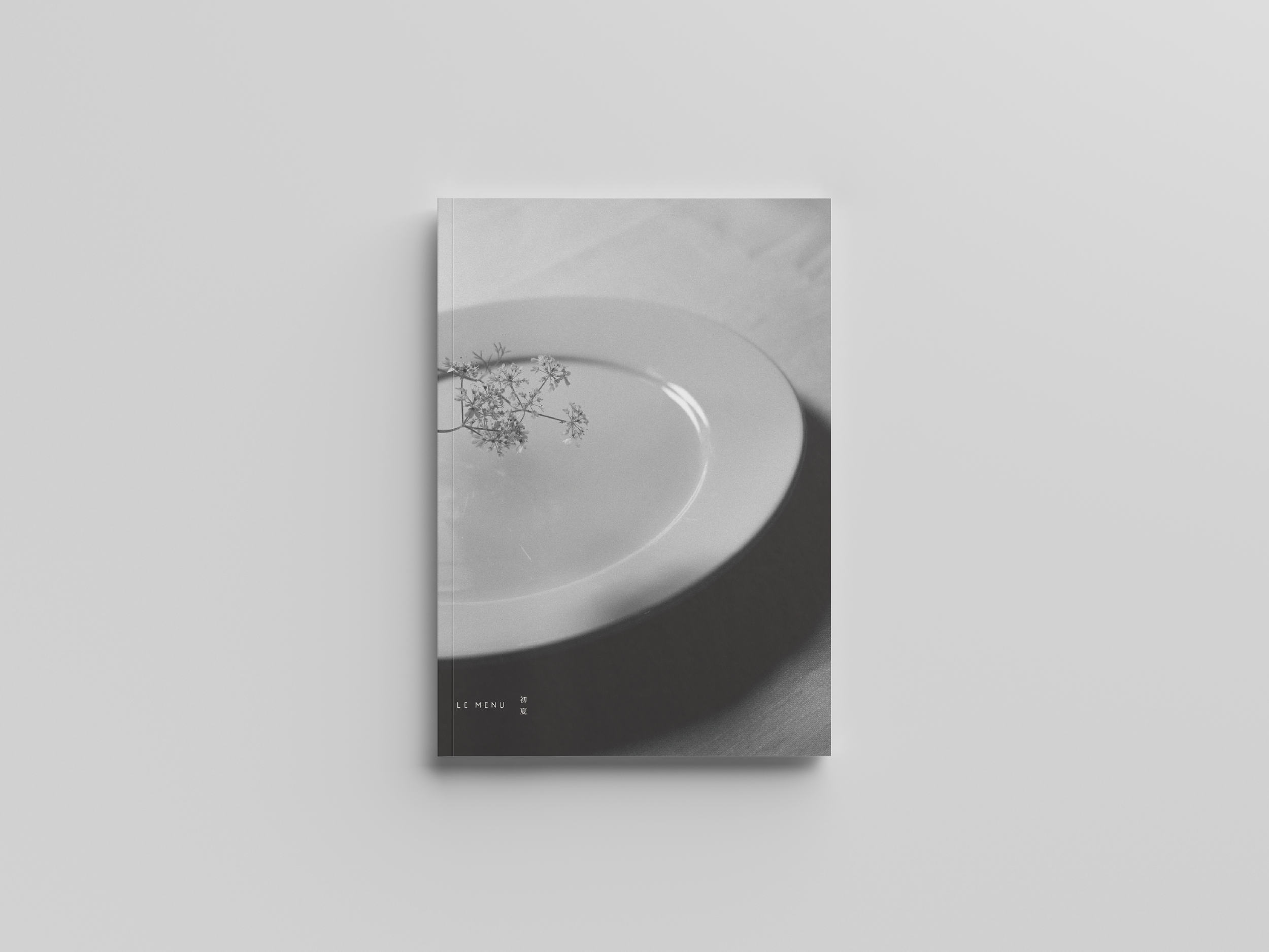 白い皿の上に花が飾られ、影が落ちているシンプルなデザインのモノクロの雑誌表紙