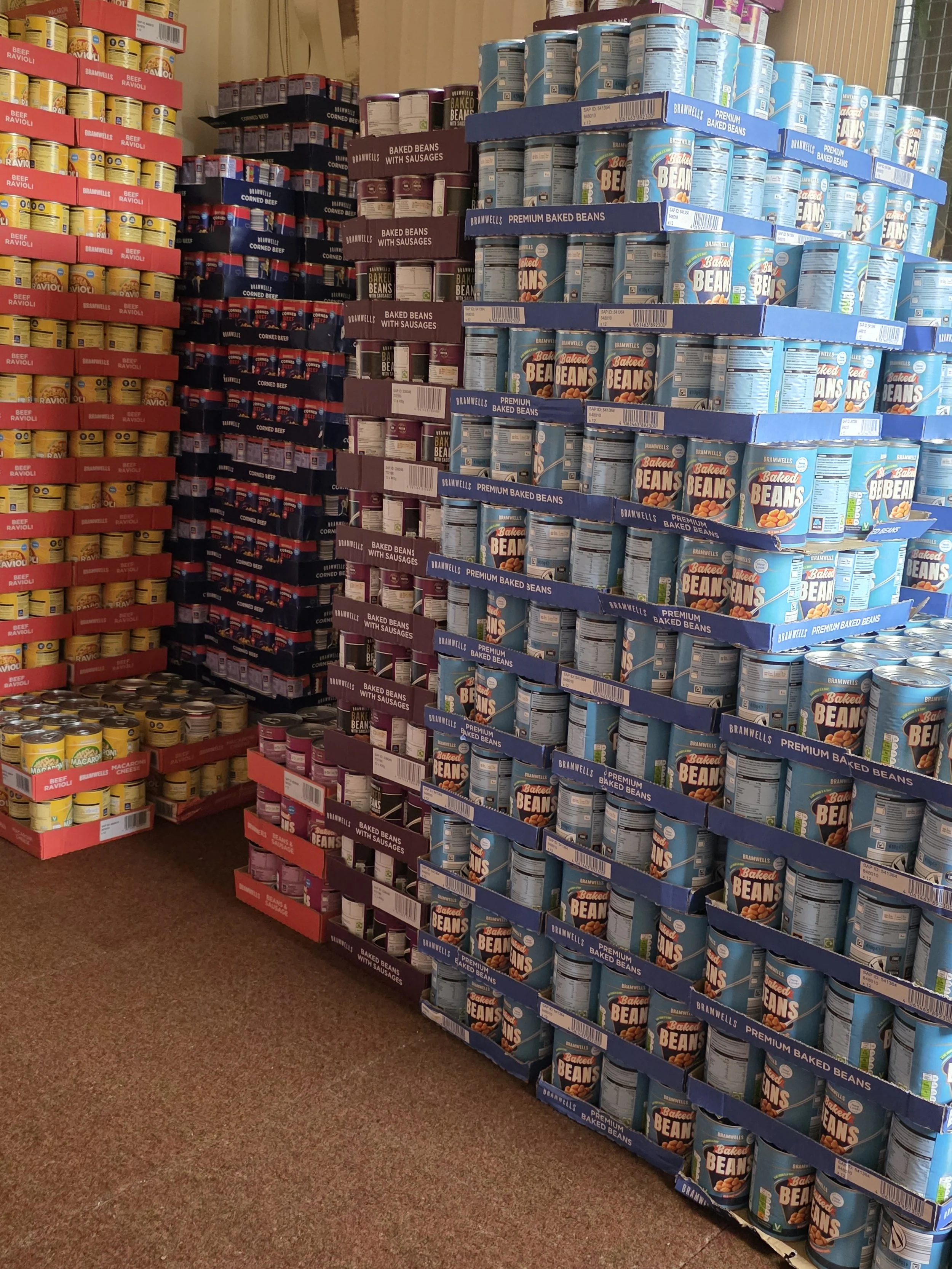 Cans of baked beans, corned beef, and beef ravioli on store shelves.