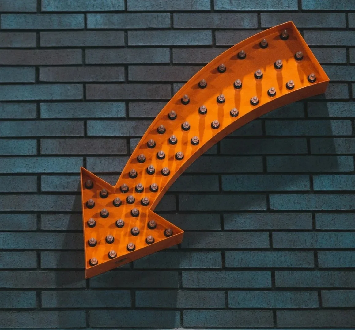 Orange arrow-shaped fixture with black bulbs on a dark gray brick wall