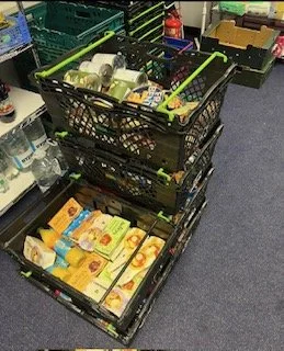 Stacked black crates containing bottled water, packaged snacks, and various grocery items in a store aisle.