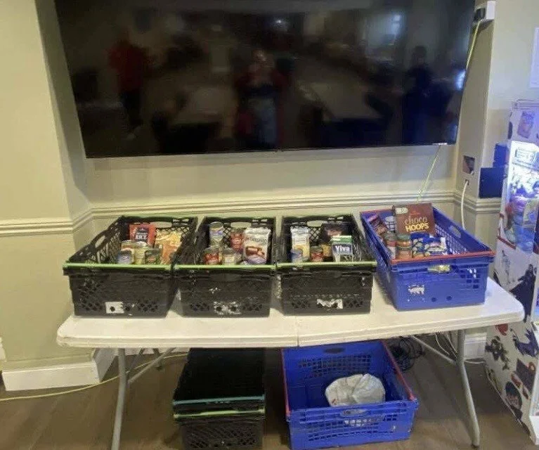 Multiple baskets of snacks and candy on a cleaning table in a room, with a large TV mounted on the wall above.