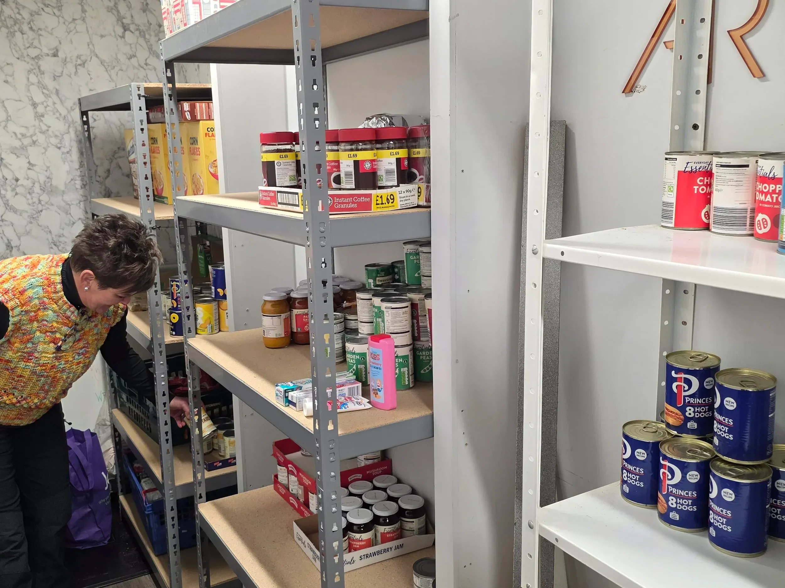 Shelving unit with canned goods and jars, a woman picking items in a pantry or storage room.