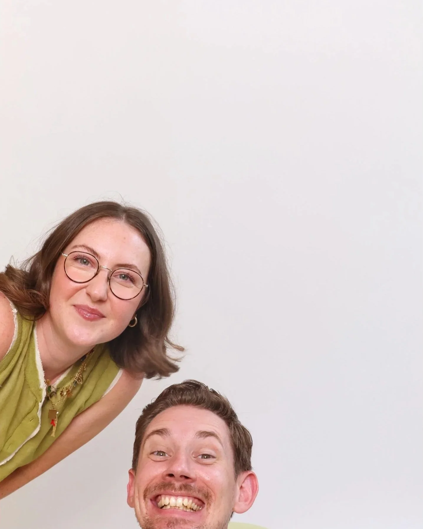 A woman with glasses smiling and a man with a big smile, both appearing happy, against a plain white background.