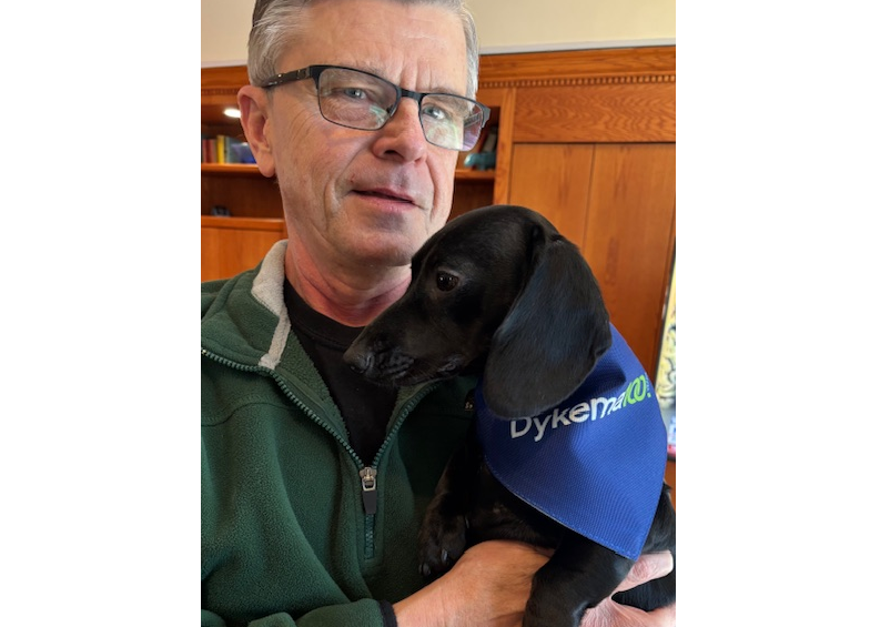 Dykema member showing off his Dachshund dressed in Dykema100 Swag