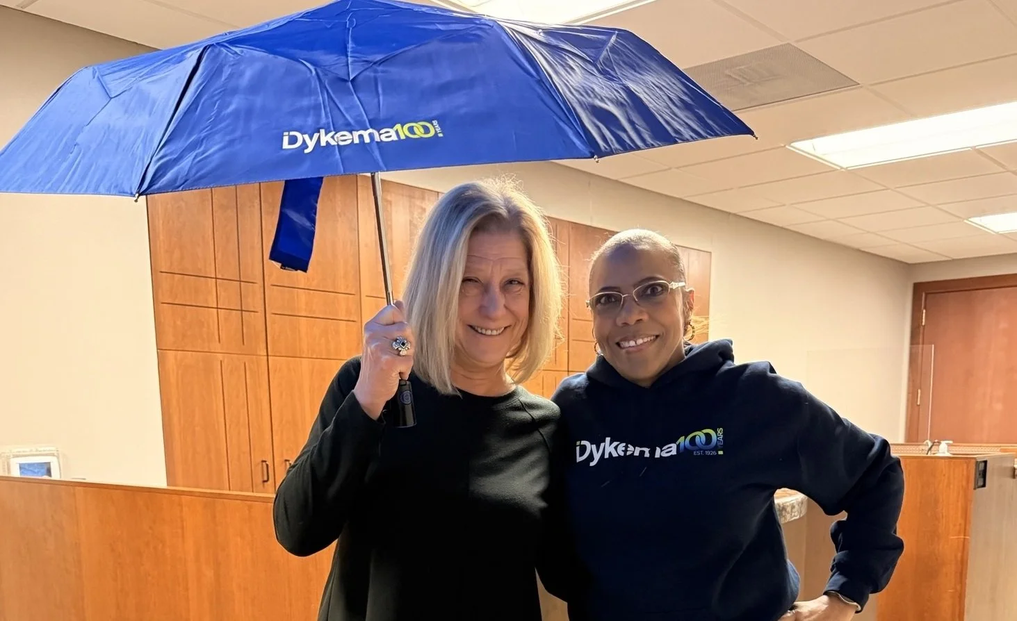 Dykema Staff showing off Dykema100 umbrella and sweatshirt 