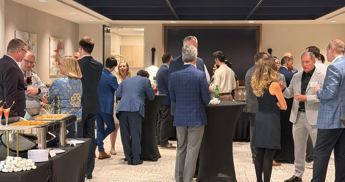 People socializing at a professional networking event with food and drinks, in a conference room with abstract art on the walls.