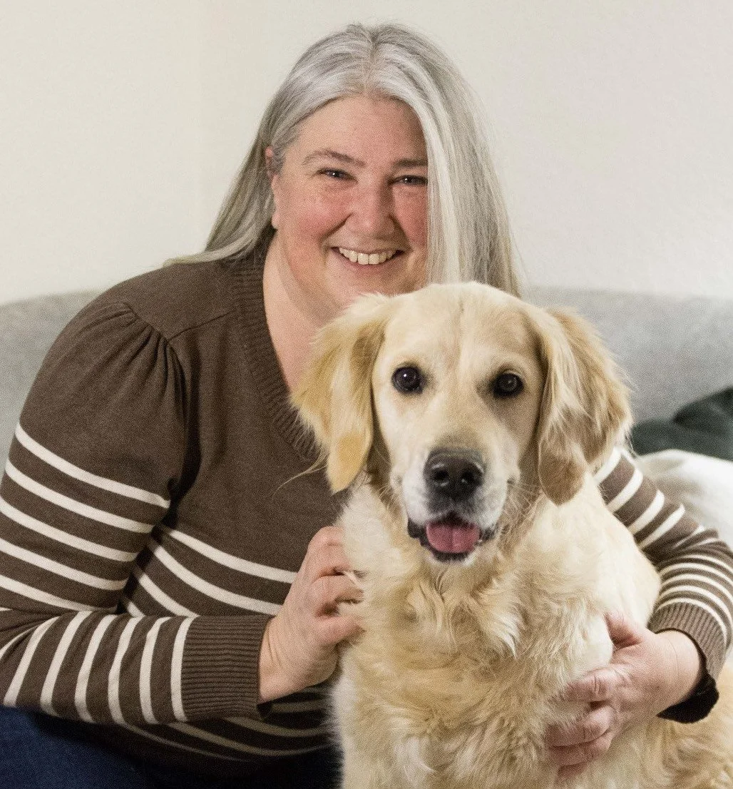 Eine lachende Frau mit grauem Haar, die ein gelbes Hund auf ihrem Schoß hat.