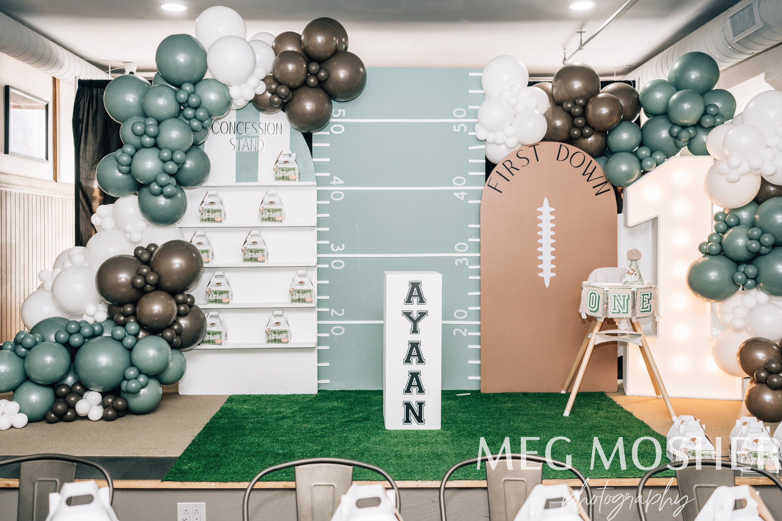 Party decoration with balloon arch, gift boxes on shelves, a large birthday sign with the name Meg, and a concession stand