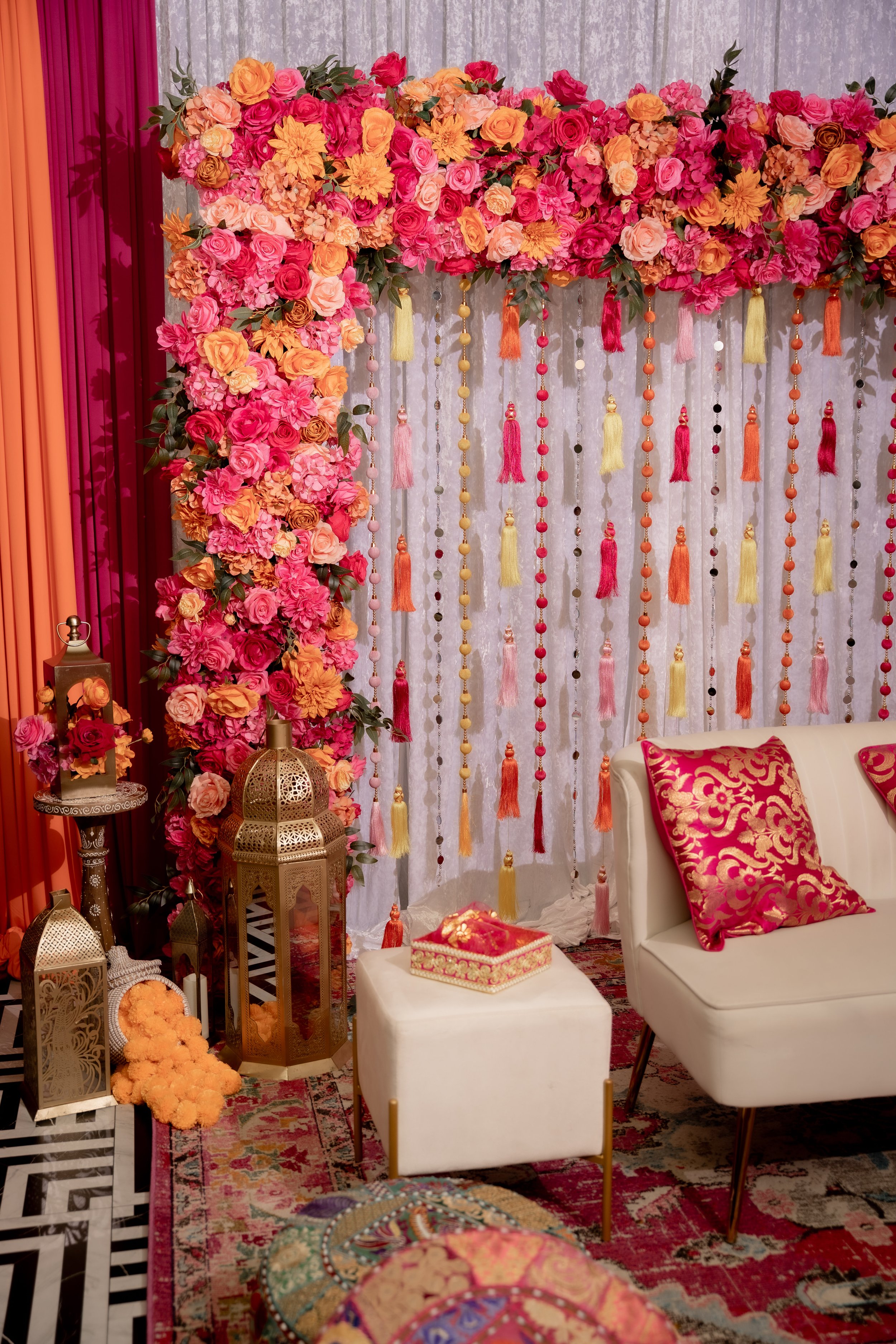 Decorative setting with a floral backdrop, patterned pillows, and ornate lanterns, likely for a celebration or event.