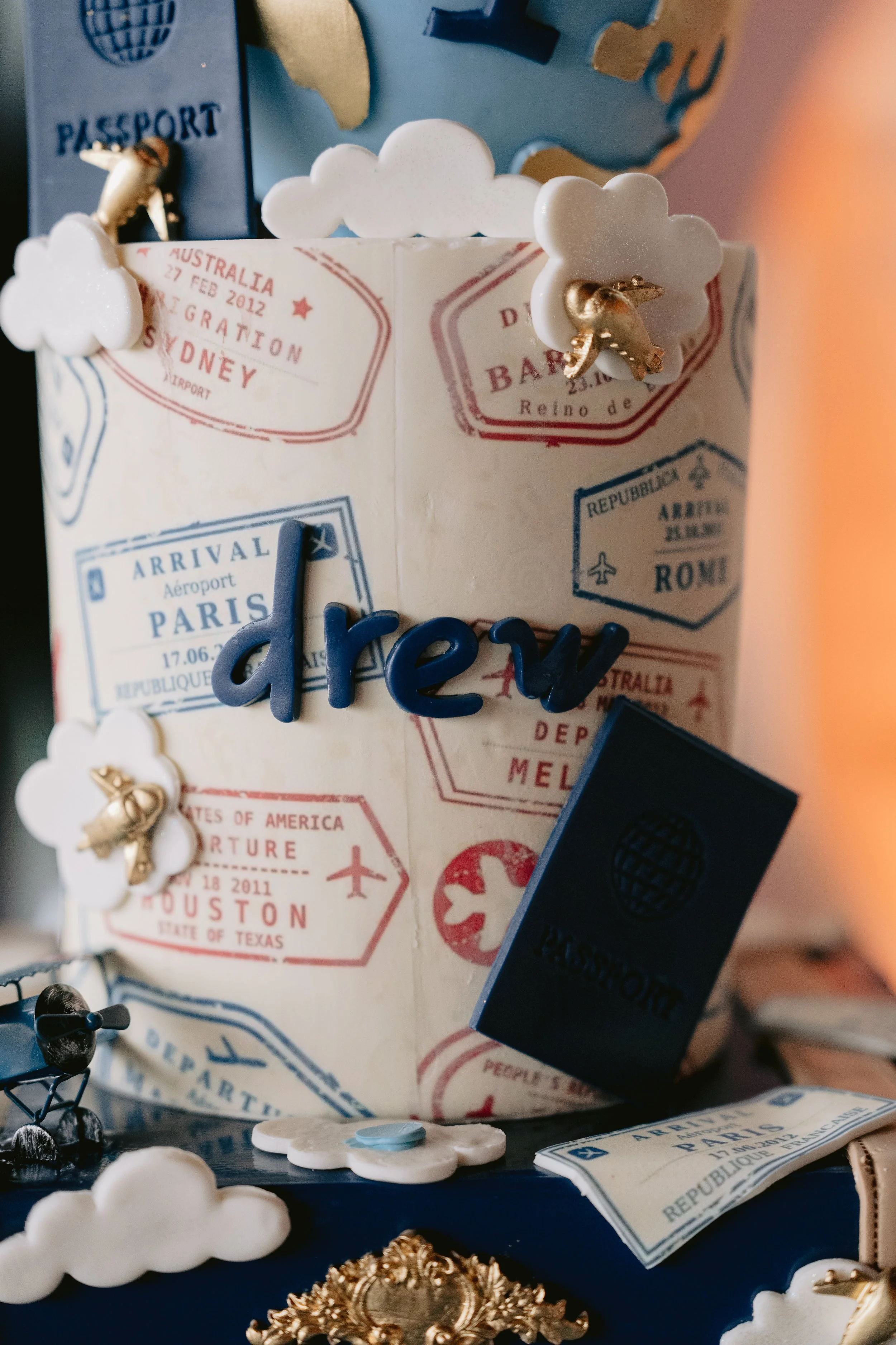 Decorative travel-themed display with miniature white clouds, blue and gold accents, miniature passport replicas, and travel stickers indicating destinations like Paris, Rome, Sydney, and Houston.