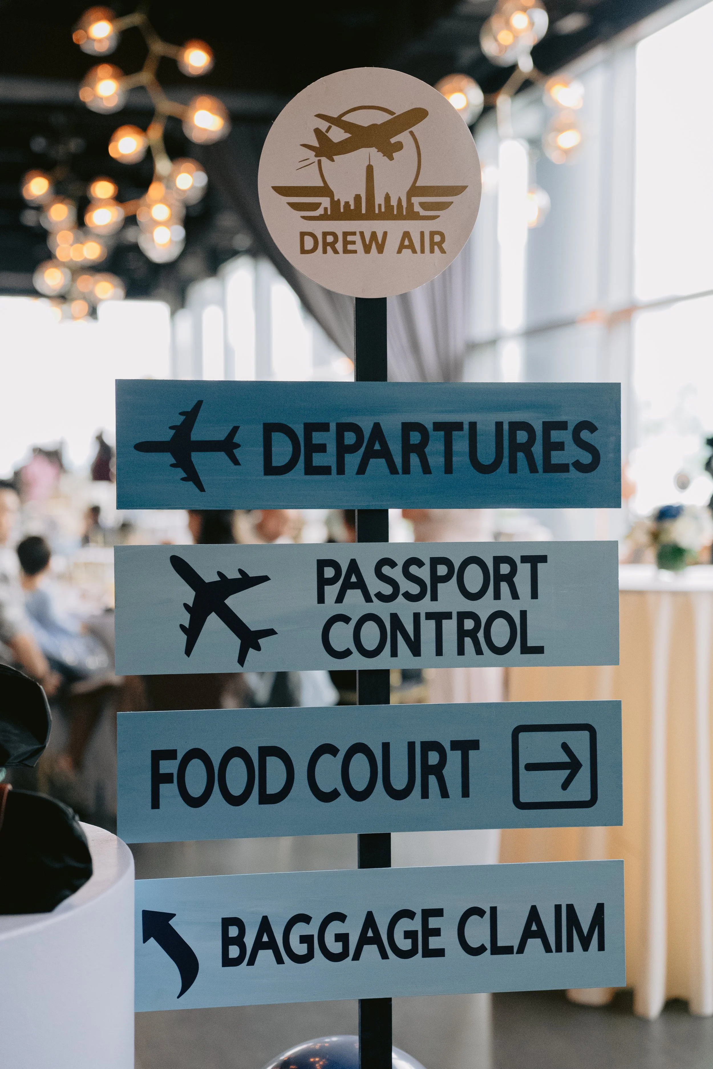 Signage at airport with four signs: Drew Air departure, passport control, food court, and baggage claim, with silhouettes of airplanes.