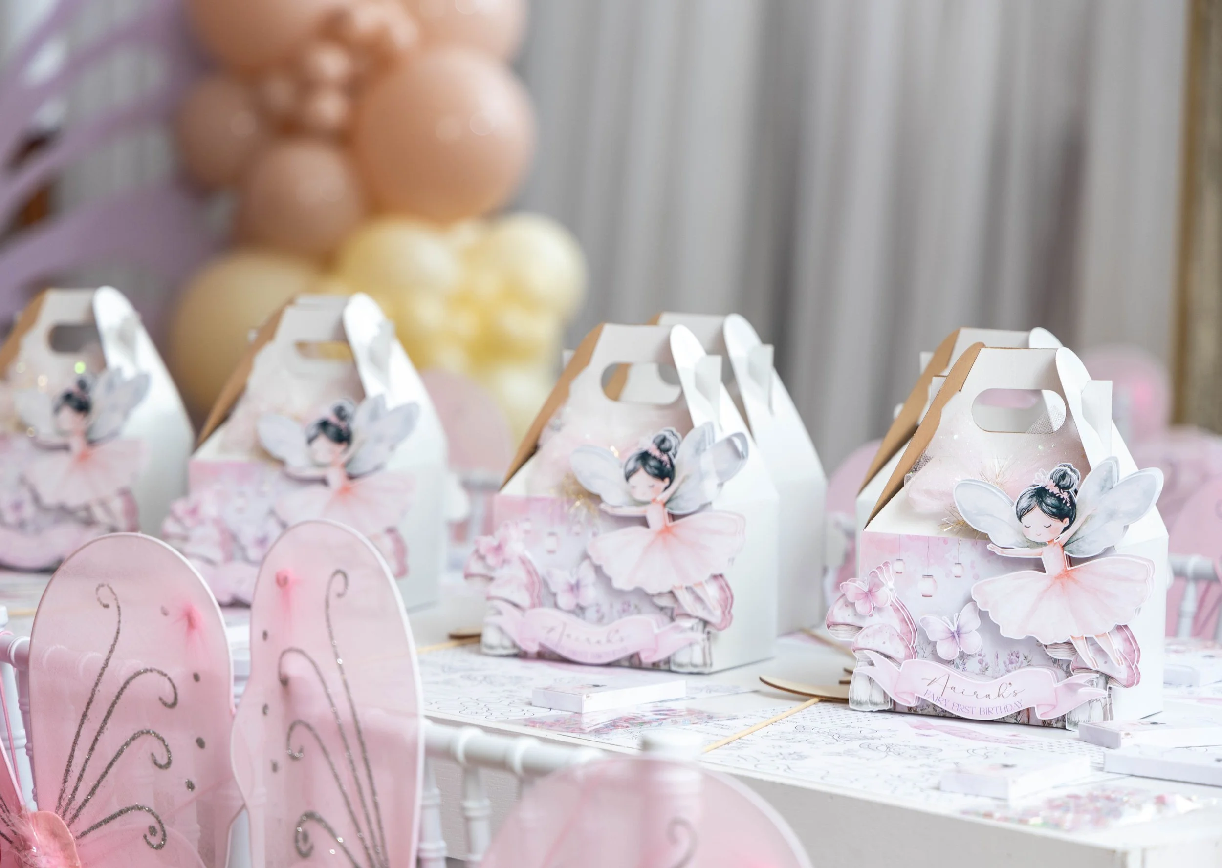 Pink fairy princess party decorations including butterfly-shaped cupcakes, favor boxes with princess illustrations, and birthday signs, likely for a child's birthday celebration.