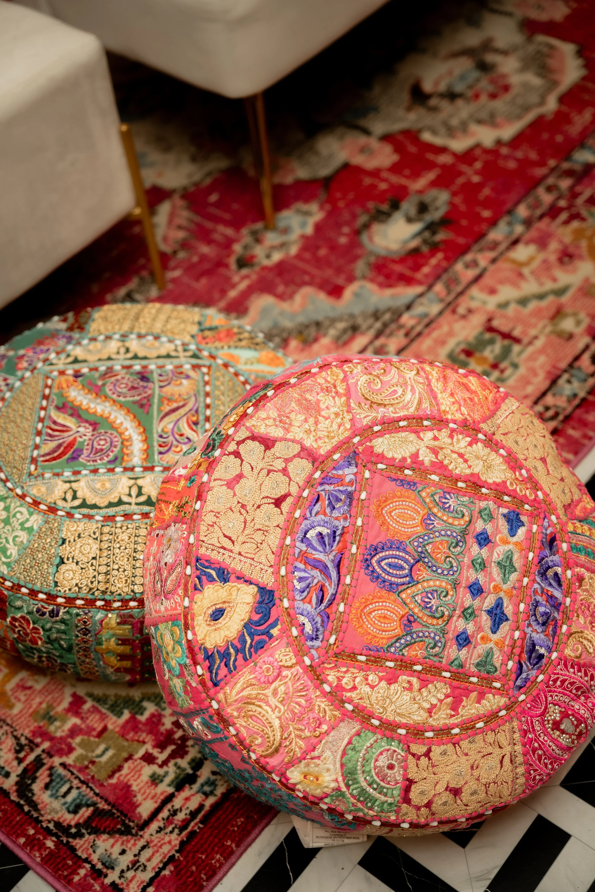 Colorful embroidered cushions with intricate patterns resting on a patterned rug and tiled floor.