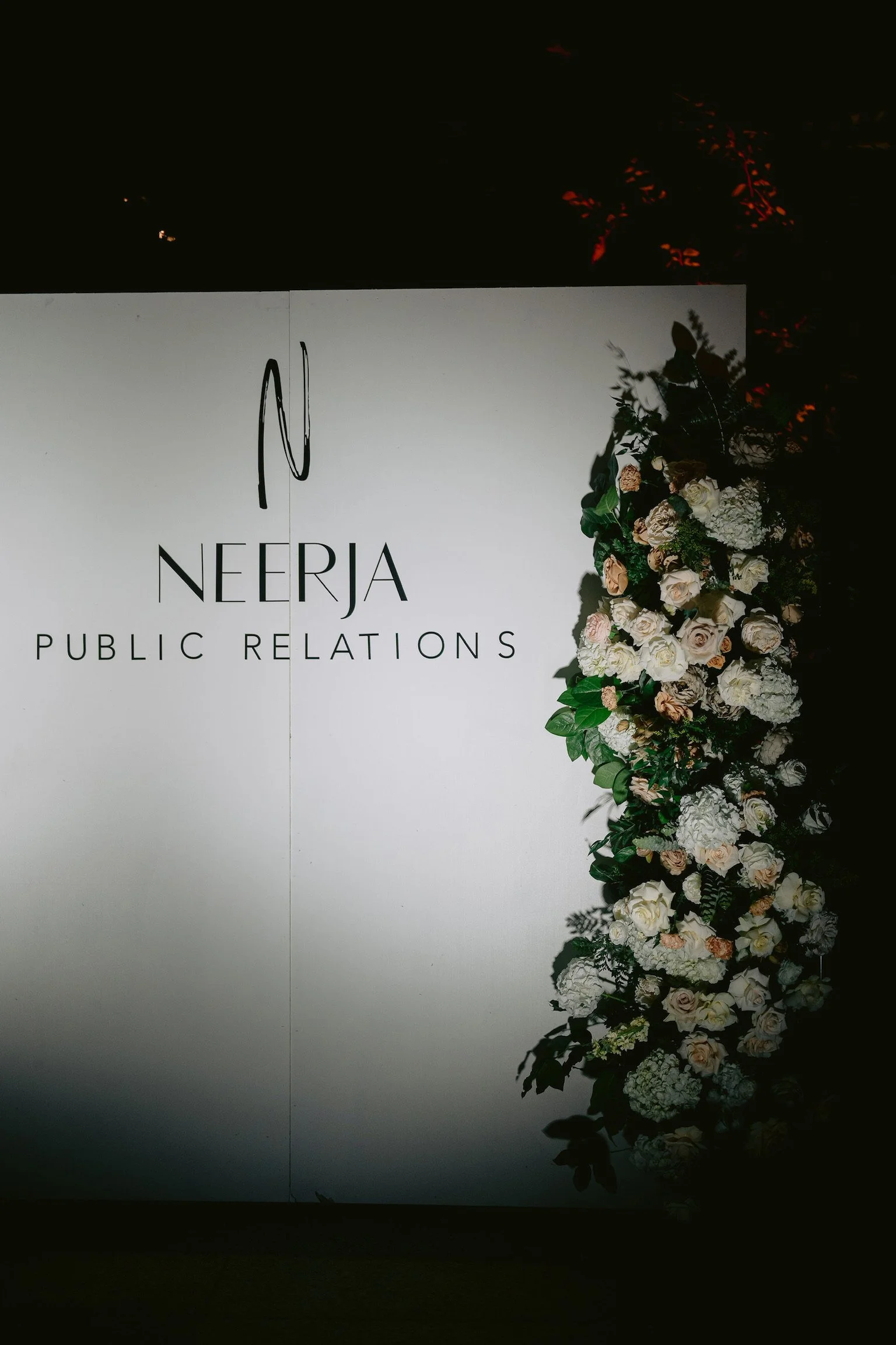A white board with the text 'Neerja Public Relations' and a floral arrangement of white and light pink roses with green leaves on the right side.