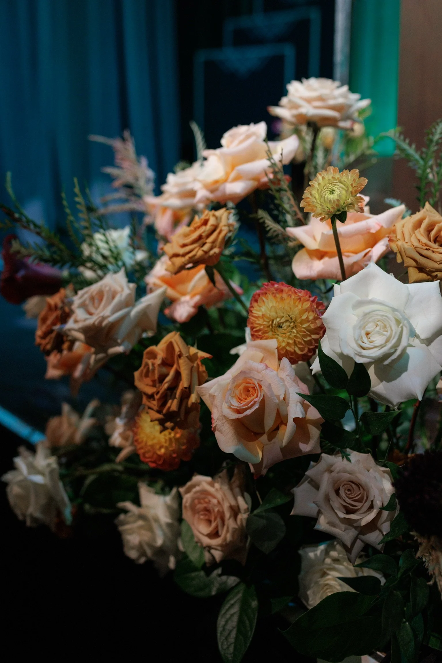 A large bouquet of cream, beige, and peach roses with some yellow and orange flowers, set against a dark background.