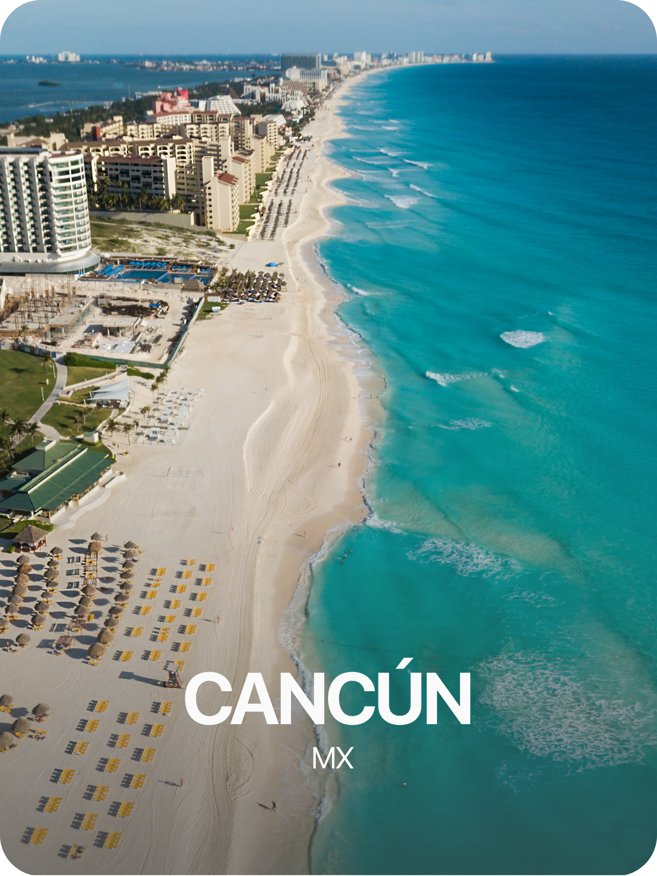 Vista aérea de la playa de Cancún, con arena blanca, olas en el mar turquesa y edificios turísticos en el fondo.