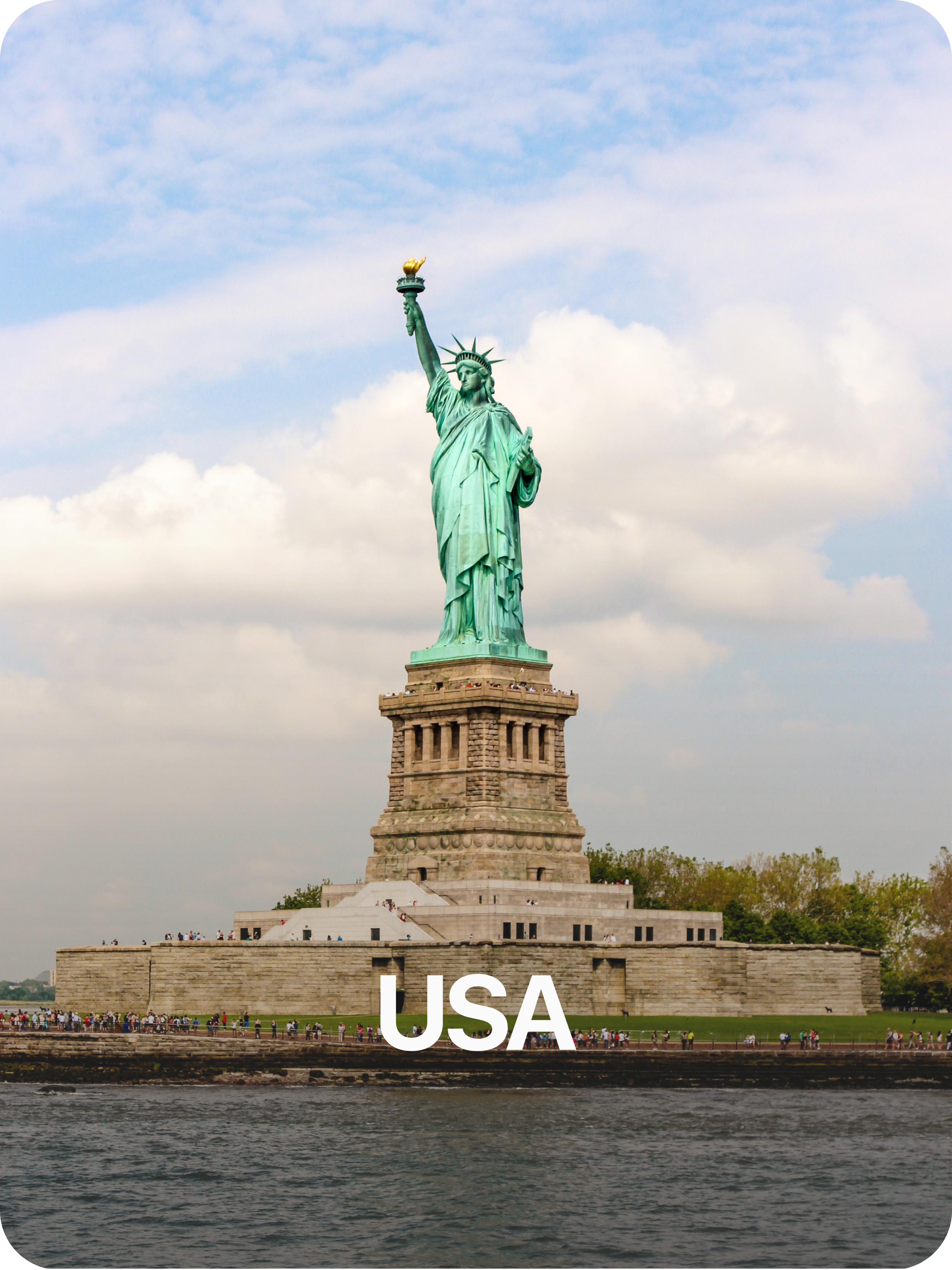 Estatua de la libertad en Nueva York, Estados Unidos, sobre una base de piedra, con agua en primer plano y cielo con nubes al fondo.