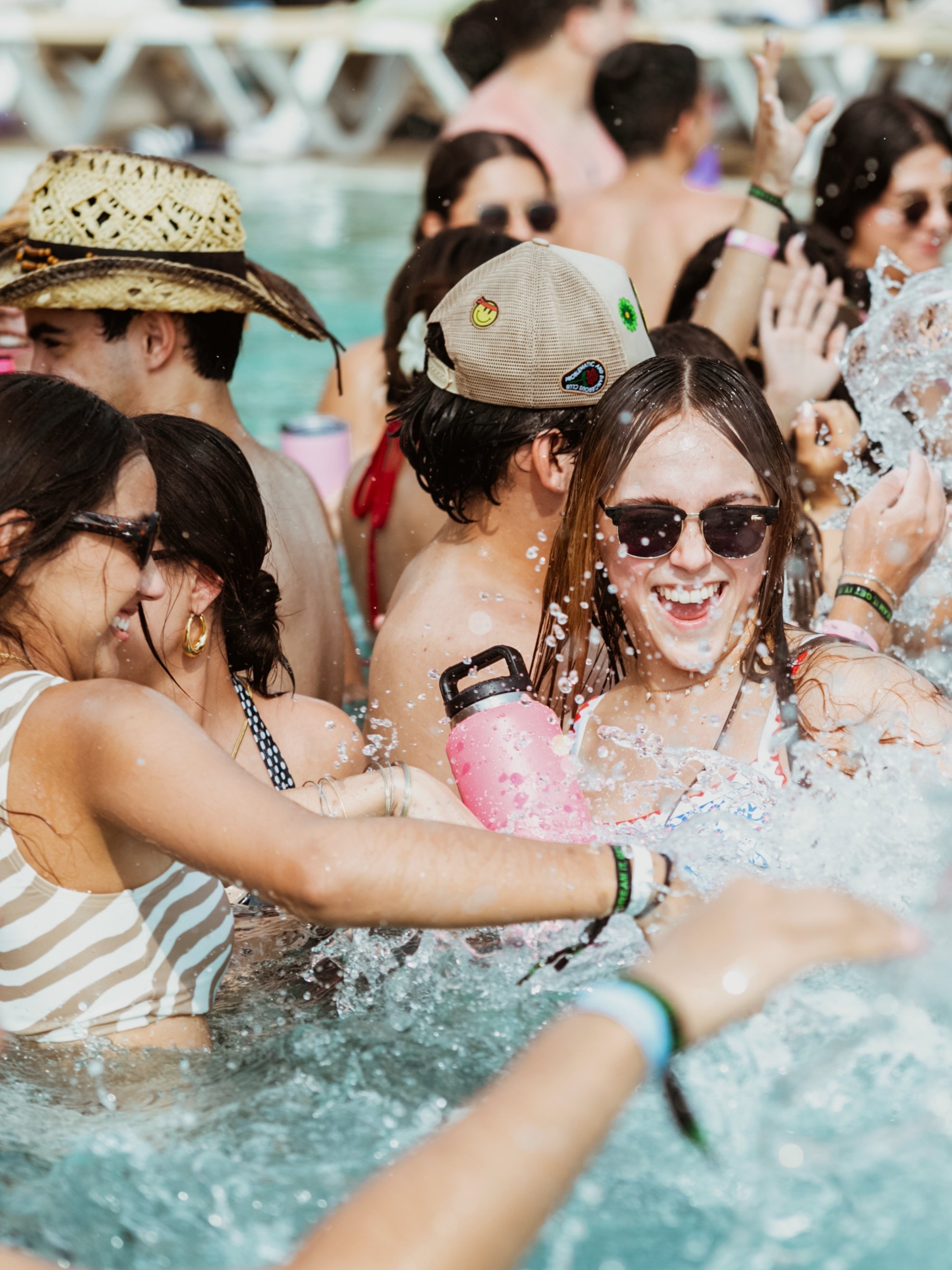Grupo de personas disfrutando y jugando en una fiesta en una piscina, con sonrisas y agua chapoteando.