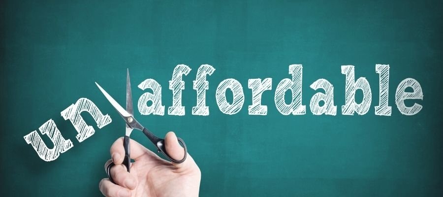 A person holding scissors cutting through the word "unaffordable" on a green background, symbolizing making something affordable.