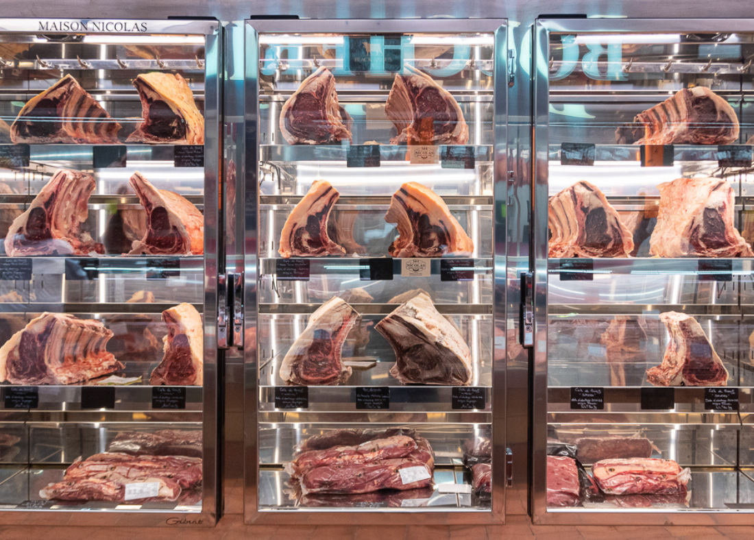 Cave de maturation contenant différents morceaux de viande, principalement des côtes de bœuf et d'autres pièces de viande rouge.