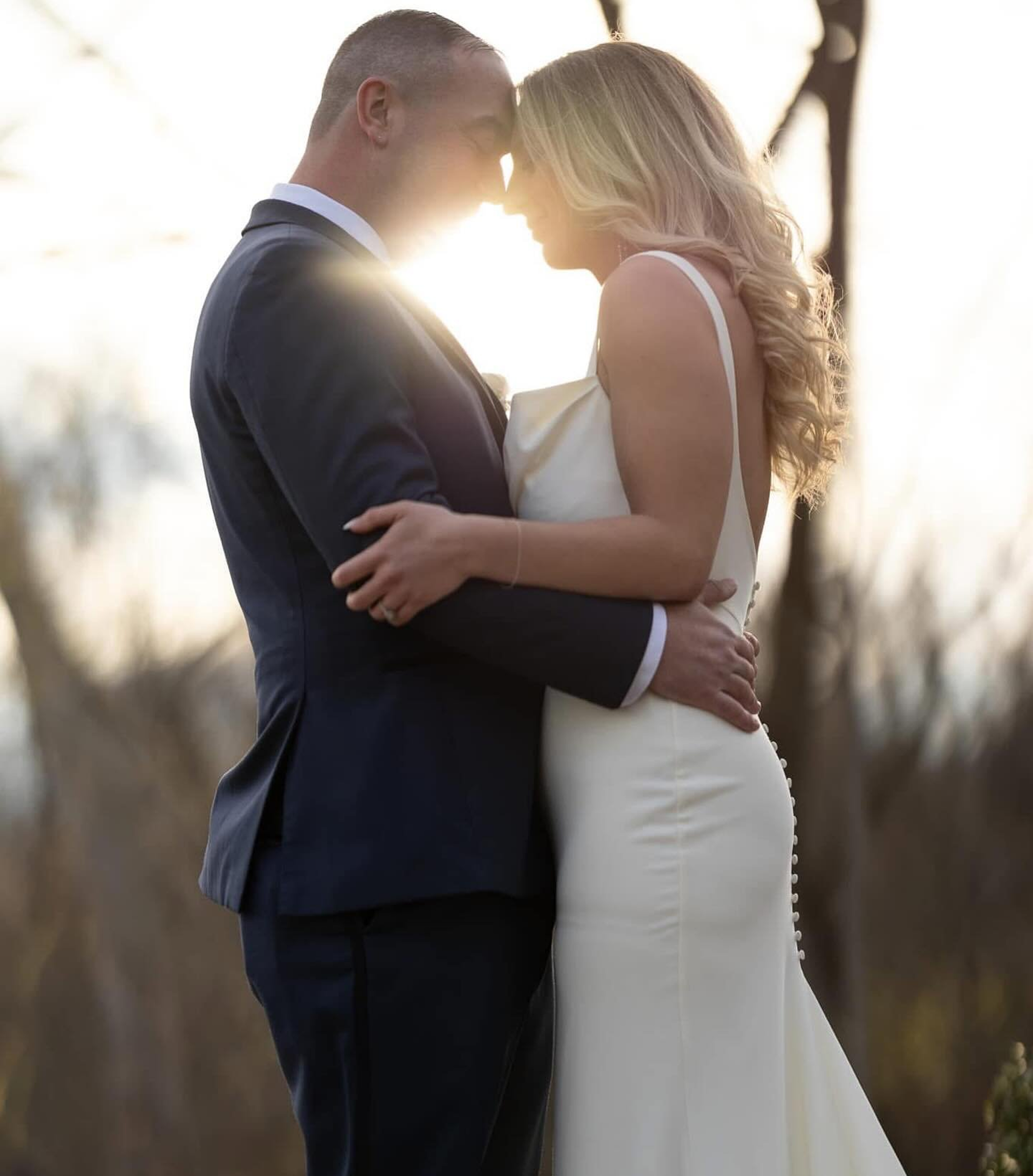Wedding couple embracing outdoors at sunset, with their foreheads touching.