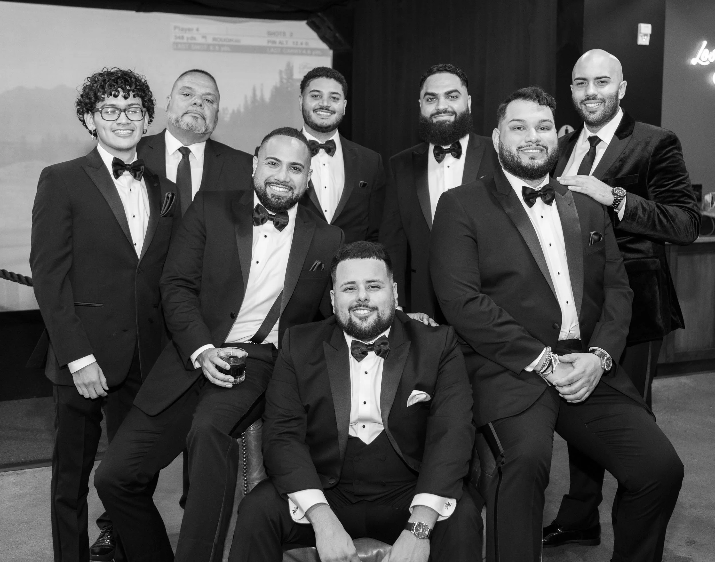 Group of men dressed in formal suits with suspenders and bow ties, posing indoors 
