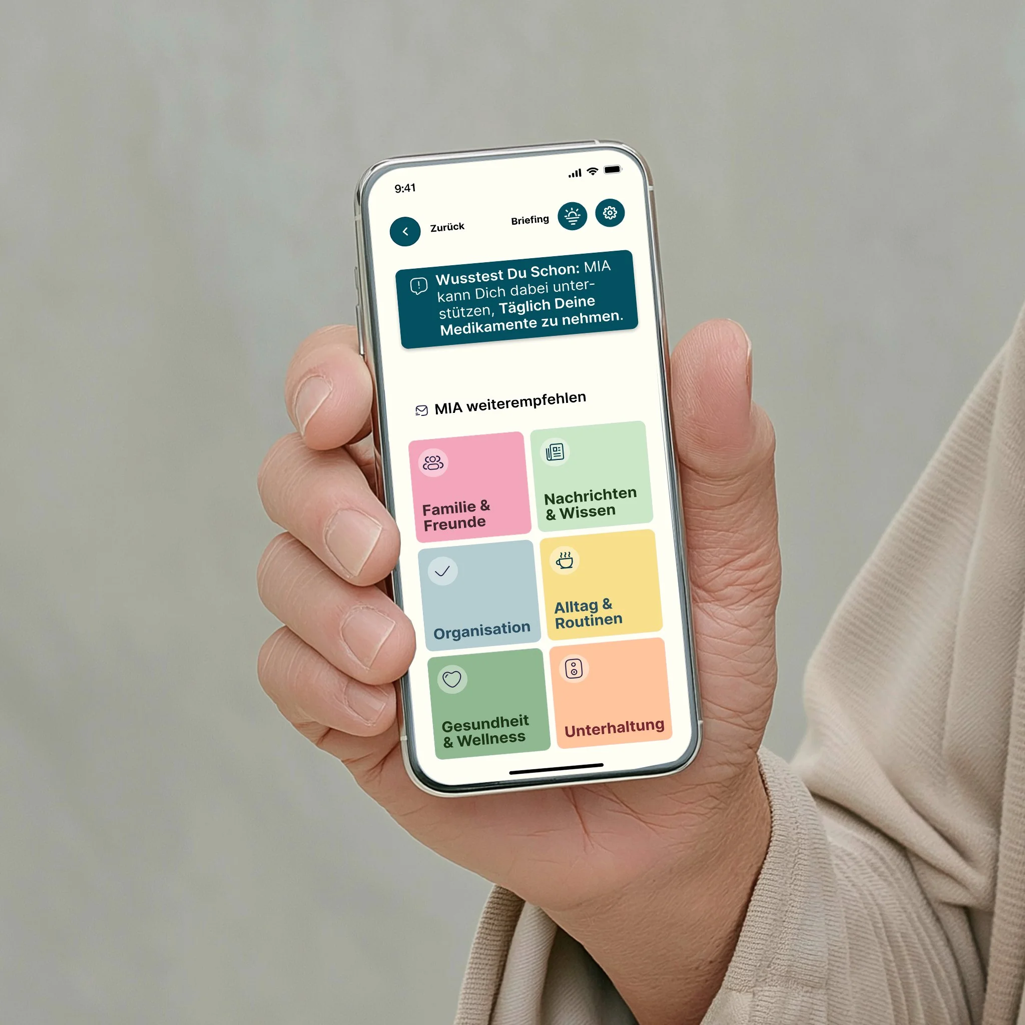 Eine Hand hält ein Smartphone mit der Amara™ App. Auf dem Bildschirm sind Kategorien wie Familie, Nachrichten, Organisation, Alltag, Gesundheit und Unterhaltung zu sehen.