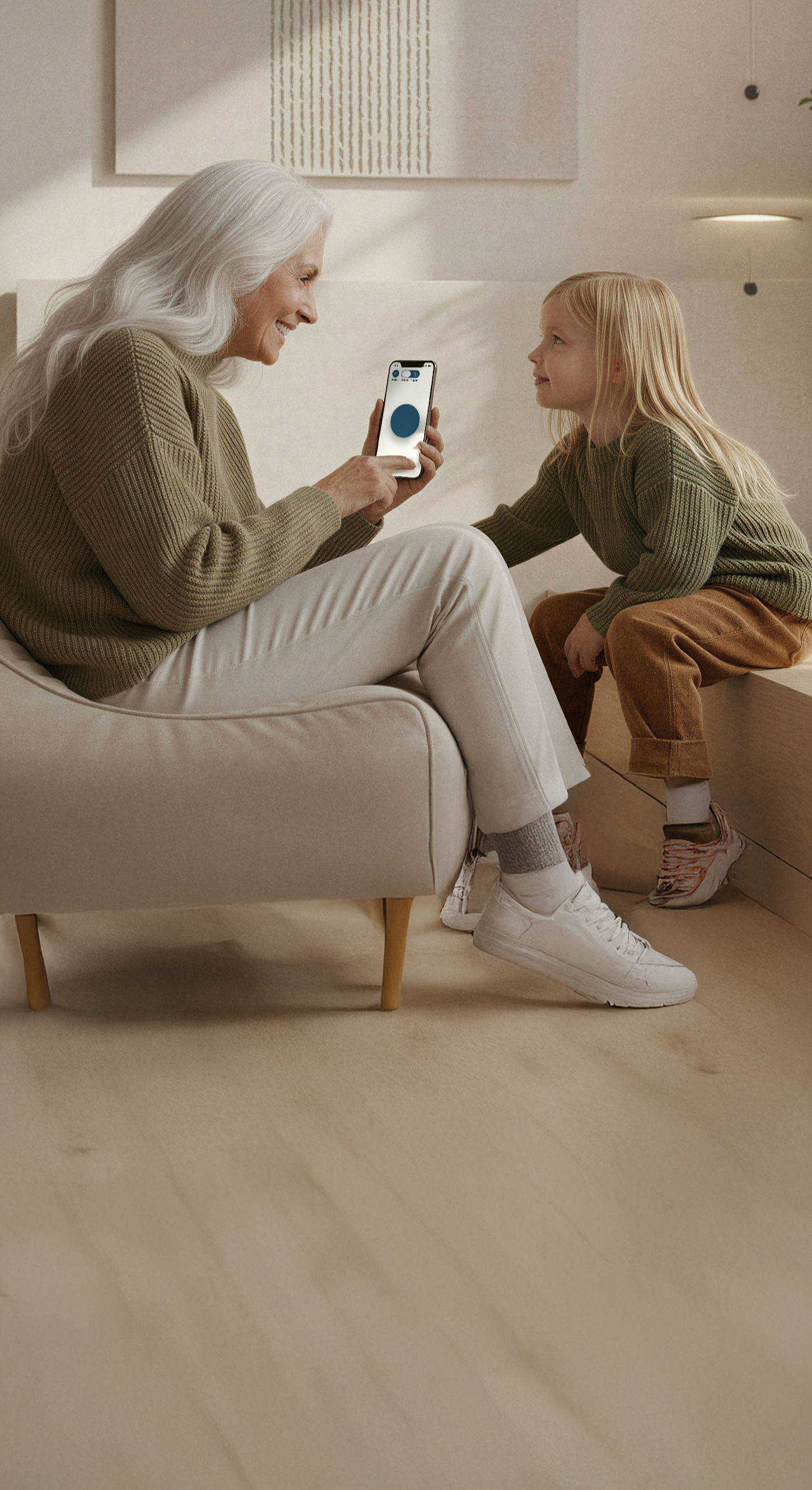 Eine ältere Frau und ein junges Mädchen sitzen auf einem Sofa in einem modernen Raum. Die Frau hält ein Smartphone in der Hand, während das Mädchen ihnen zuschaut.