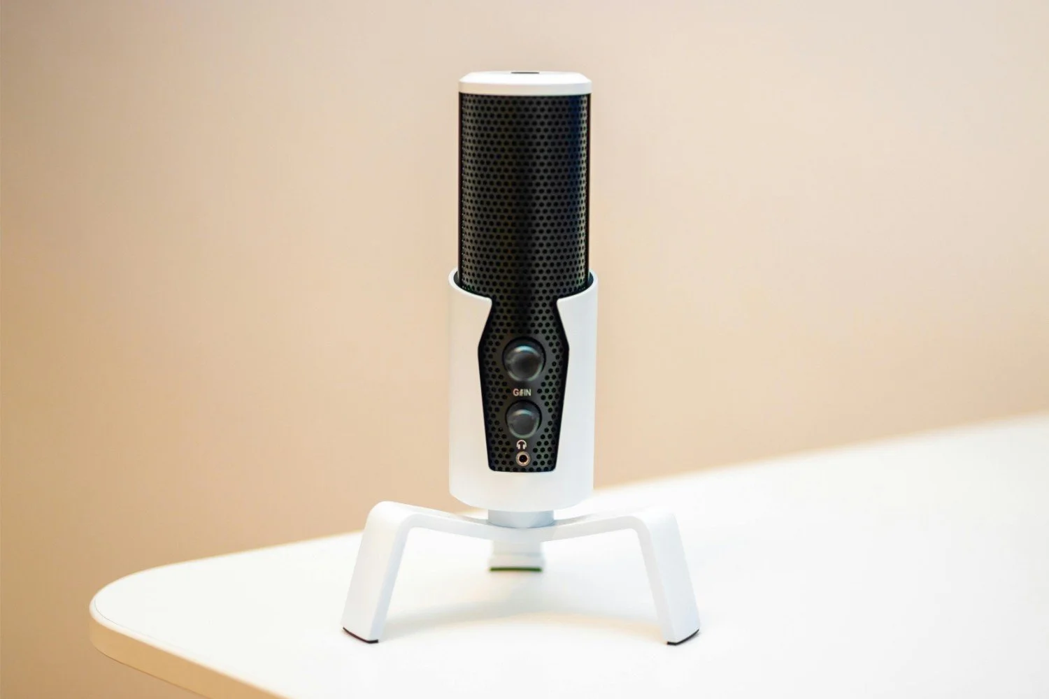 A modern microphone with a black and white design, positioned on a white surface against a beige background.