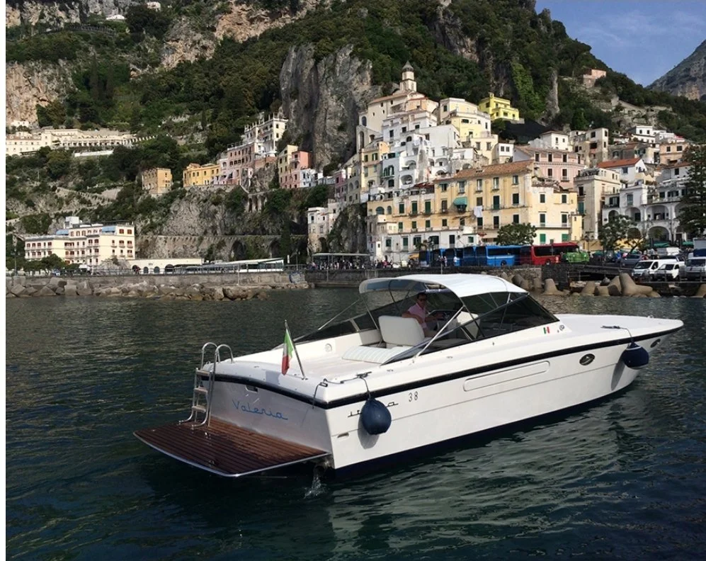 A white motorboat on the water near a hillside town with colorful buildings stacked on steep terrain.