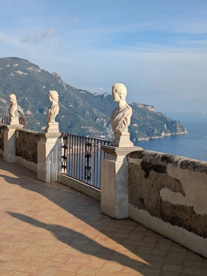 View of the infinity terrace in villa Cimbrone with balustrades and bust sculptures overlooking a coastal landscape with mountains and sea.