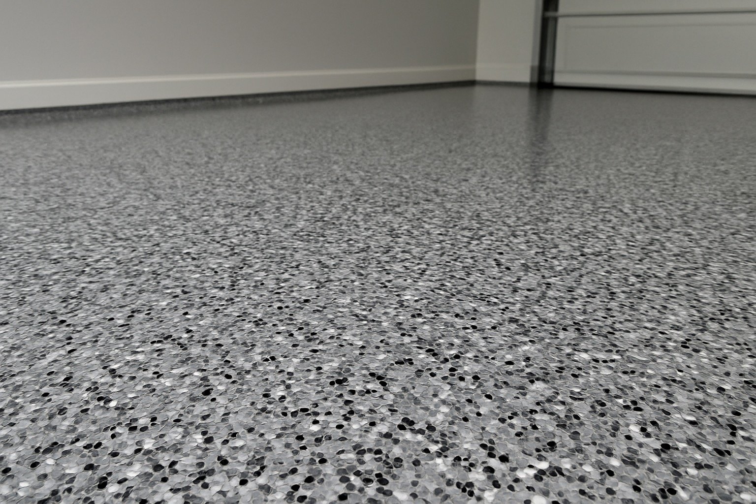 Close-up of a gray speckled epoxy floor in a room with white walls and a gray garage door.