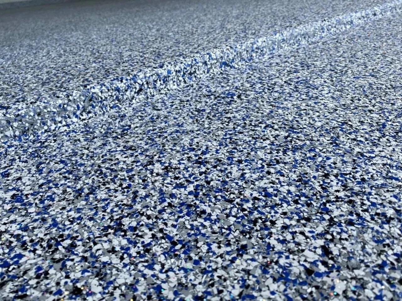 Close-up of a textured epoxy surface with multicolored blue, white, and black confetti-like particles.