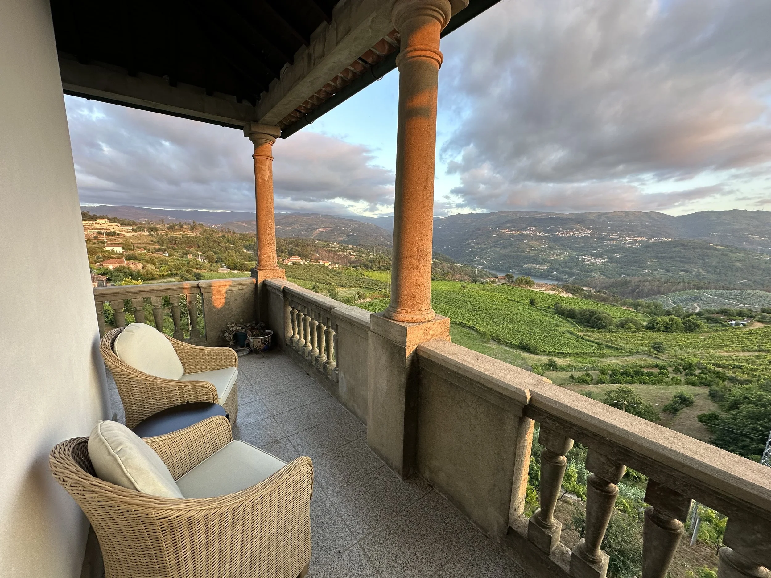Two wicker chairs on the back terrace at Casa Belo Horizonte overlooking Douro vineyards, the river, and mountains at sunset.