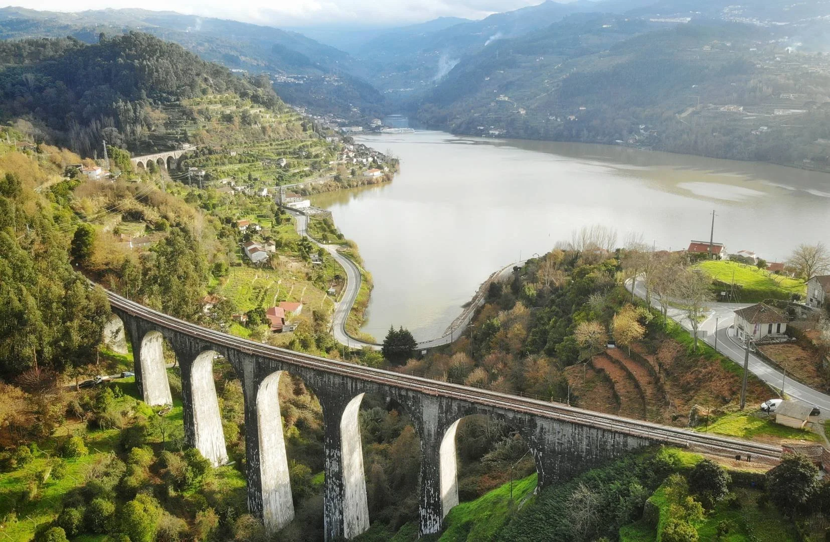 Railway bridge along the Douro Train Line crossing the river through terraced hills and farmland.