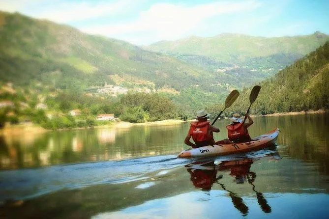 Two people kayaking on a calm Douro river surrounded by green hills.