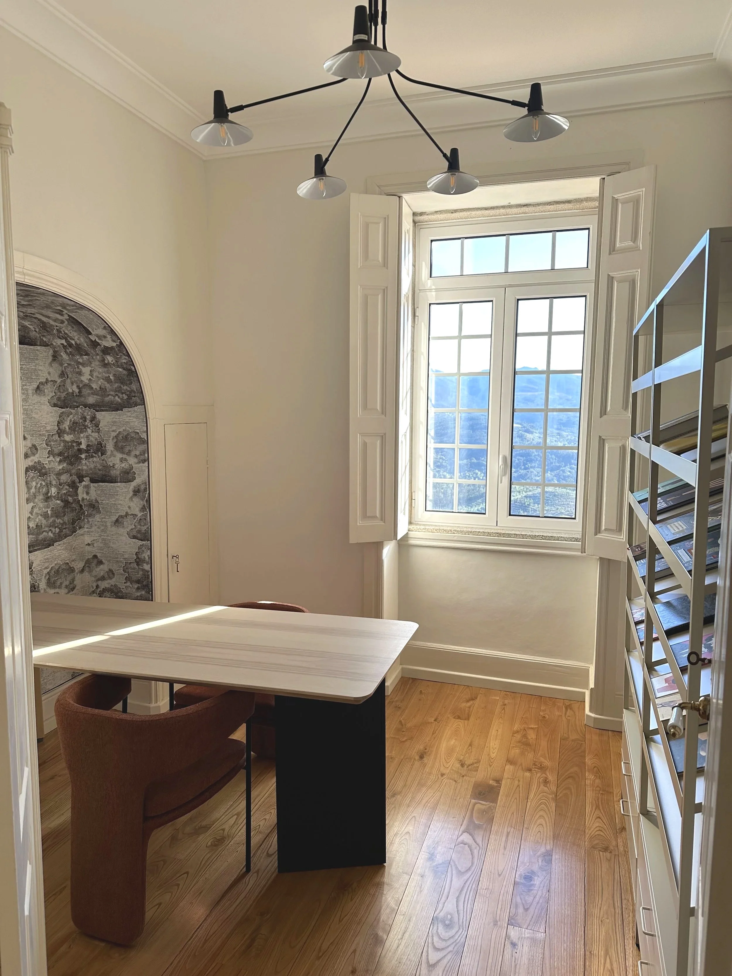 Office library at Casa Belo Horizonte with workspace, bookshelves, and natural light from an open window.