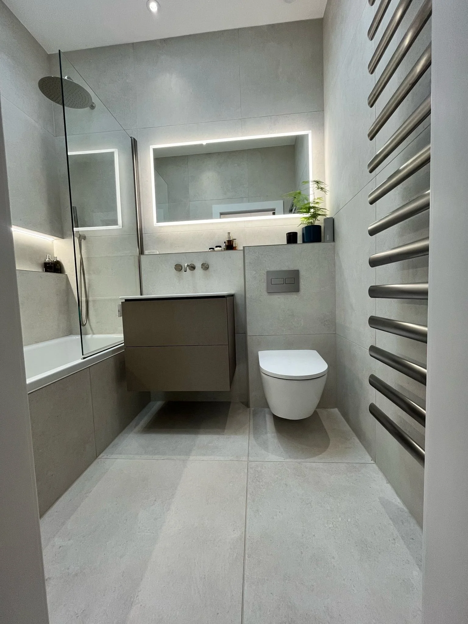 Modern bathroom with a shower area with a glass partition, a wall-mounted toilet, a floating vanity with a mirror above, and a heated towel rail on the wall.
